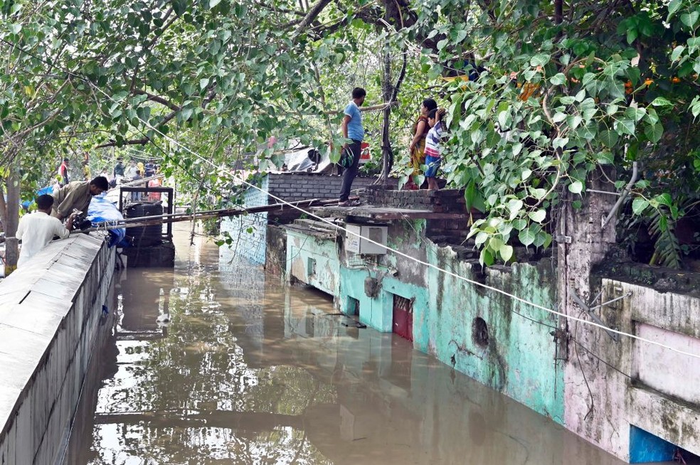 Moradores esperam nos telhados de casas inundadas enquanto o nível da água do rio Yamuna sobe devido a fortes chuvas na Índia — Foto: Getty Images