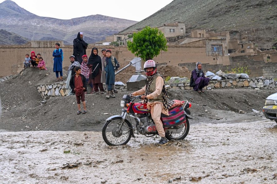 Um homem afegão dirige sua motocicleta pela água da chuva ao longo de uma estrada no vale de Tangi, no distrito de Saydabad, na província de Maidan Wardak