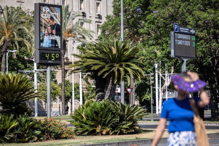 Pedestre com leque passa por um indicador de temperatura de 45°C nos jardins do Prado de San Sebastian, em Sevilha, Espanha, na quarta-feira, 5 de julho