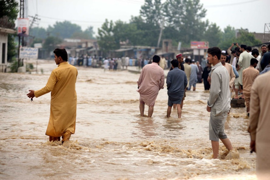 Paquistaneses atravessam água após enchente atingir o distrito de Charsadda, no noroeste do país
