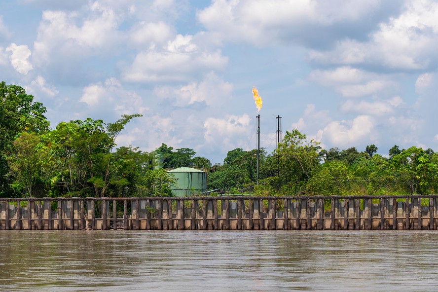 Local de extração de petróleo com chaminé para queima de gases de combustão e tanque de armazenamento ao longo do rio Napo, parque nacional Yasuni, na floresta amazônica, Equador.