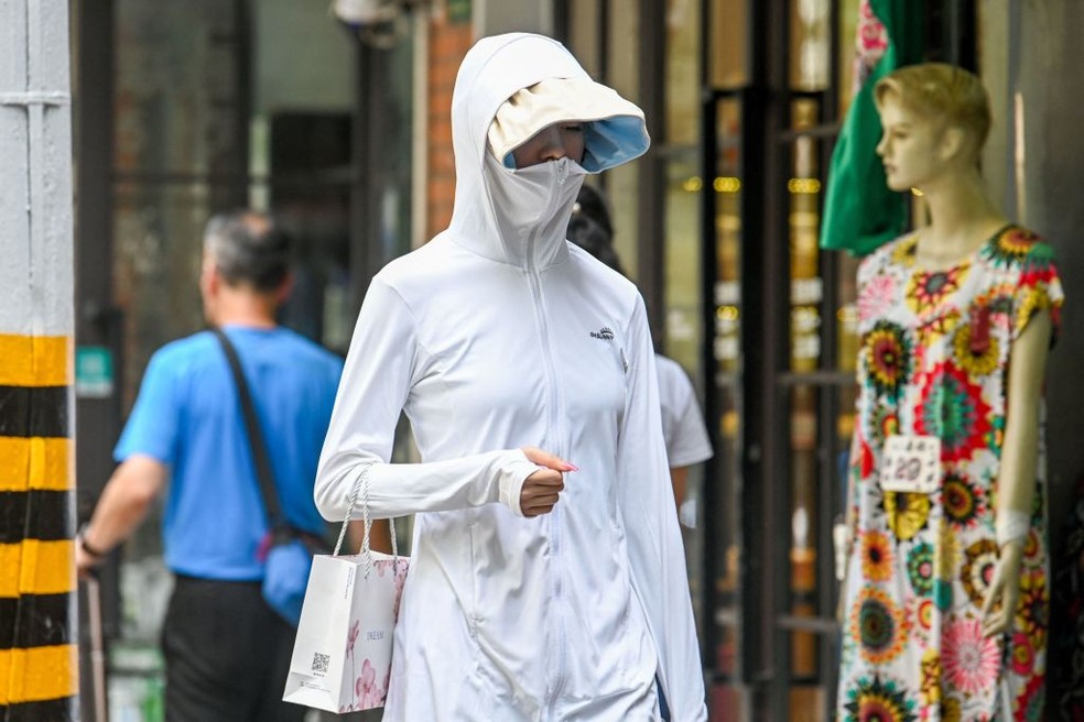 Uma mulher vestindo roupas de proteção solar caminha por uma rua em meio ao clima quente em Xangai em 29 de maio de 2023 — Foto: Getty Images