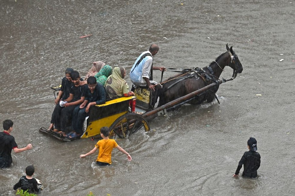Pessoas andam de carroça por uma rua inundada após fortes chuvas no Paquistão — Foto: Getty Images
