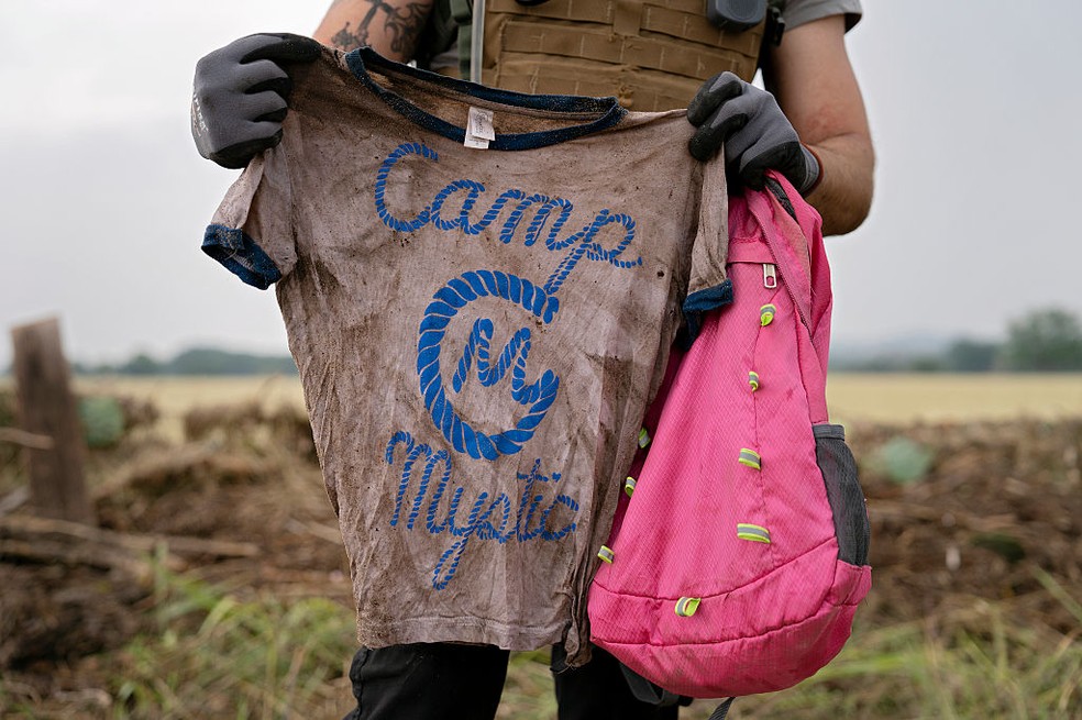 Um voluntário de busca e resgate segura uma camiseta e uma mochila com as palavras Camp Mystic em Comfort, Texas — Foto: Getty Images