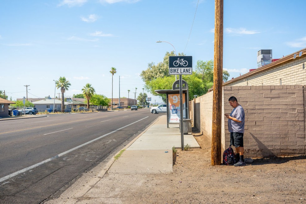 Morador fica atrás de um poste para fazer sombra enquanto espera o ônibus durante onda de calor em Phoenix, Arizona — Foto: Getty Images