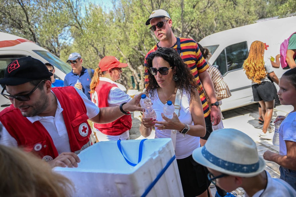 Trabalhadores da Cruz Vermelha Grega distribuem garrafas de água aos visitantes em frente à Acrópole, em Atenas, que chegou a fechar as portas nas horas mais quentes do dia — Foto: Getty Images